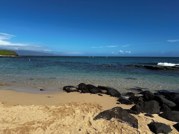 A beach with clear water, rocks, and a distant landmass.