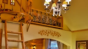 Une pièce chaleureuse avec un lit en mezzanine, une échelle en bois, un lustre, un canapé et une petite table avec une lampe.