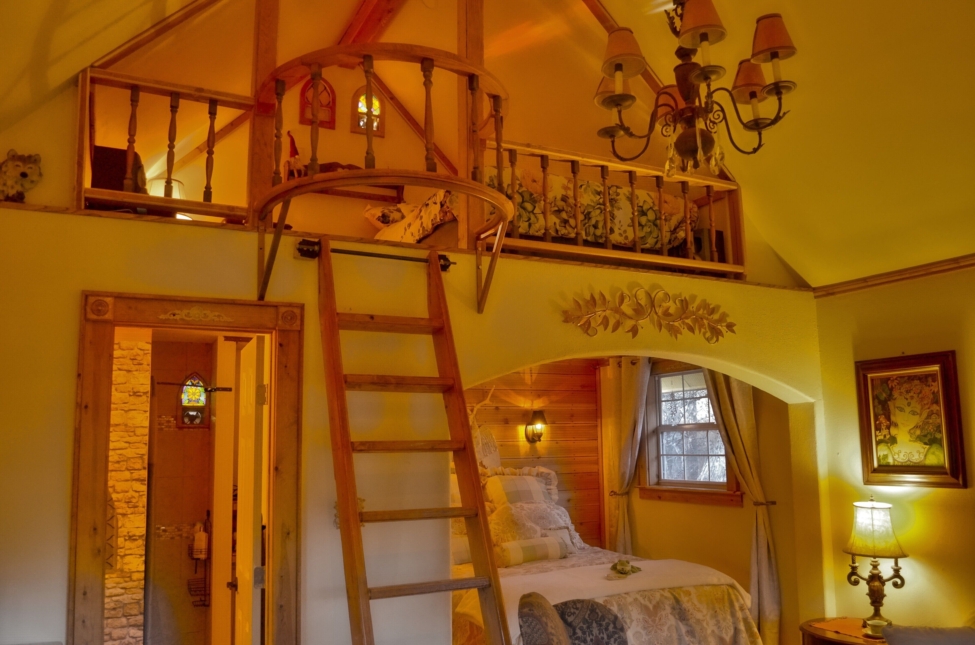 Ein Schlafzimmer mit einem Schlafpodest, einer Holzleiter, einem Chandelier und einem Buntglasfenster.