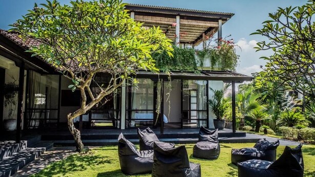 Una casa moderna con porche cubierto, mobiliario exterior y abundante vegetación.