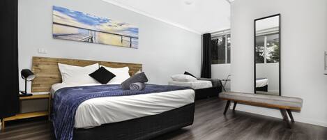A modern bedroom with a large bed, a bench, a bedside table, and a mirror.