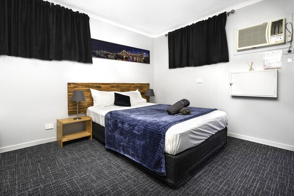Une chambre d’hôtel avec un lit, une table de chevet, une lampe, un tableau au mur et une fenêtre avec des rideaux.