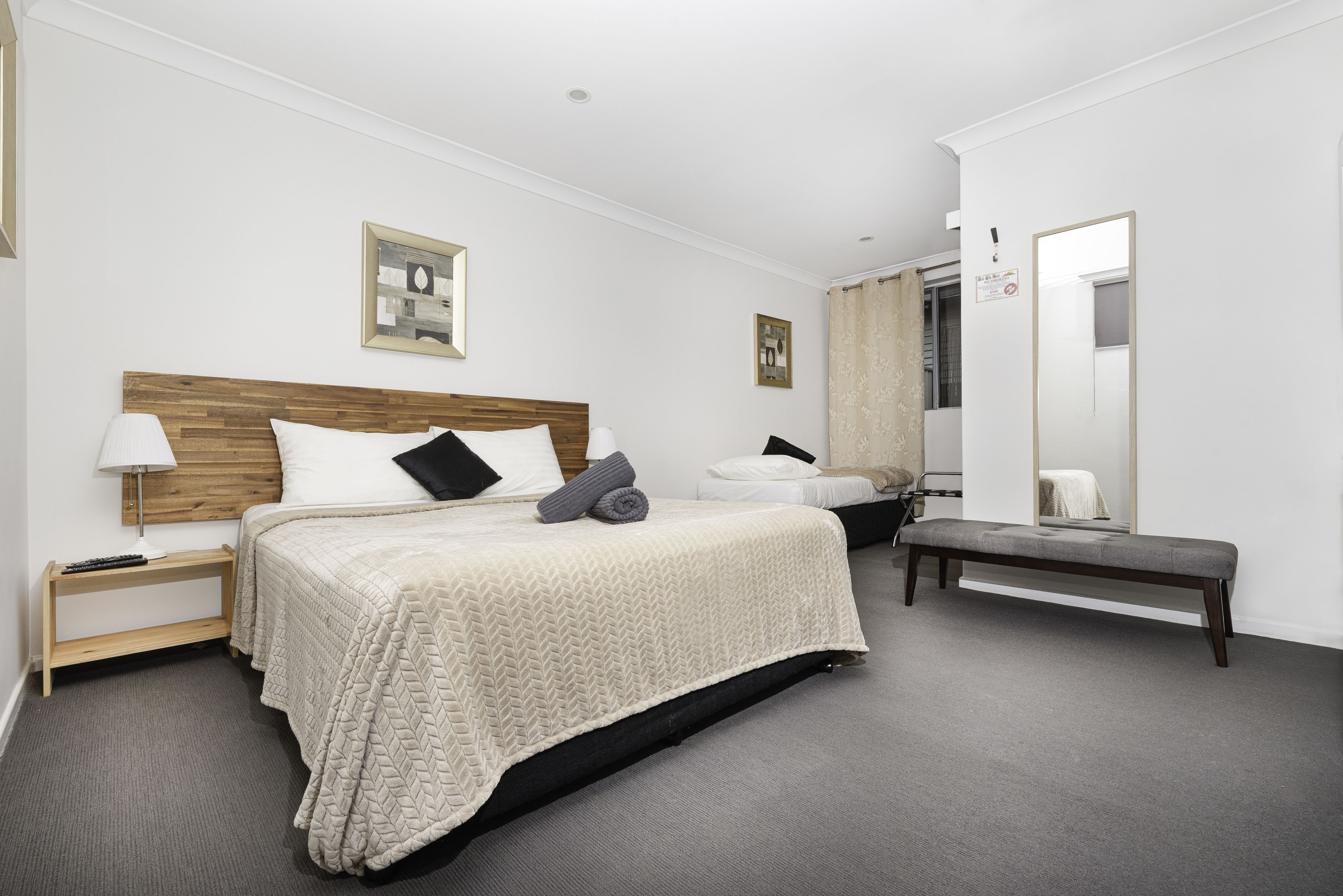 A hotel room with a large bed, a bench, a nightstand, a lamp, and a mirror.