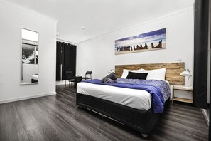 Un dormitorio moderno con una cama grande, cabecera de madera, mesita de noche, espejo y un cuadro de caballos en la pared.