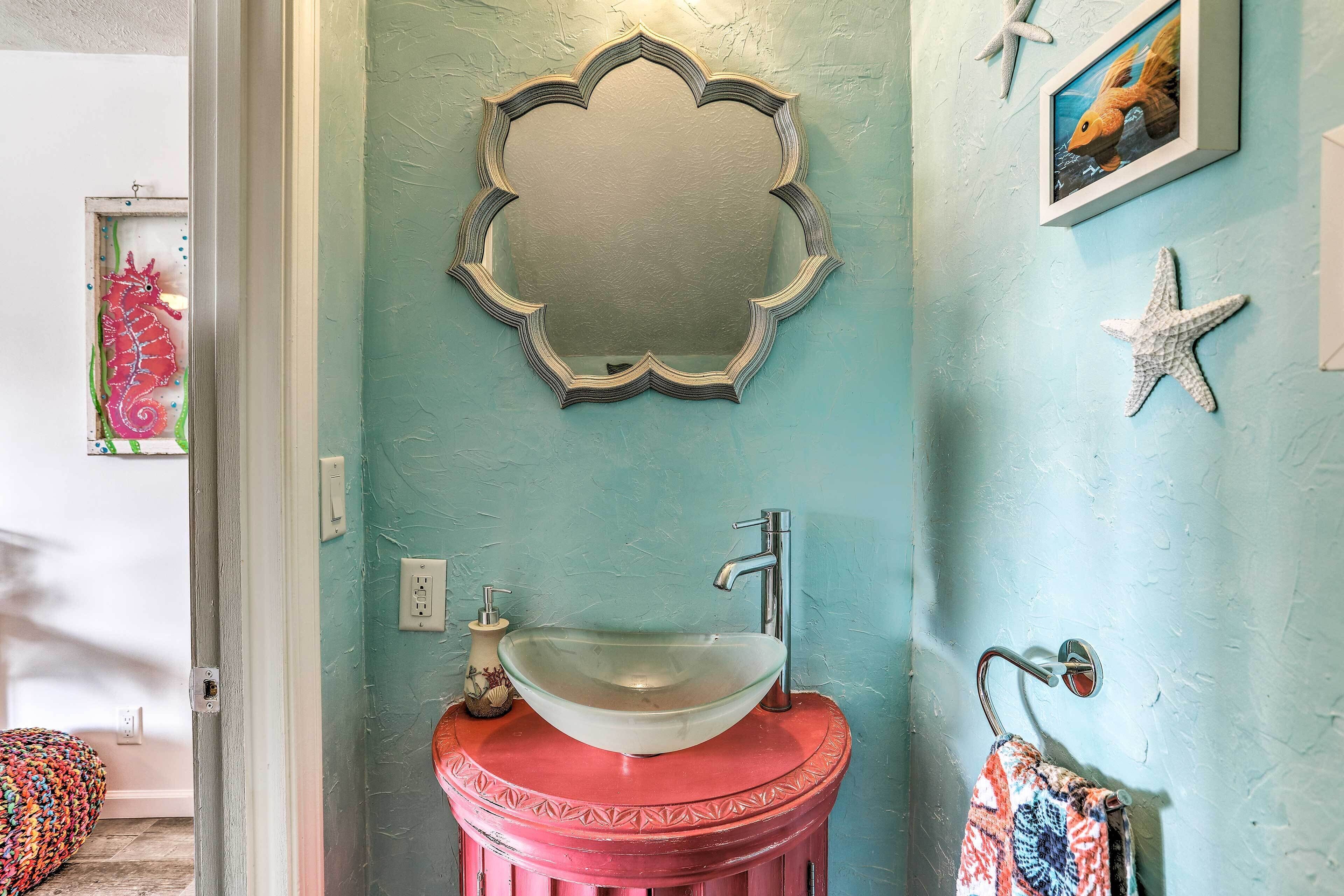 A bathroom with a round sink on a red pedestal, a mirror with a scalloped frame, and a starfish decoration on the wall.