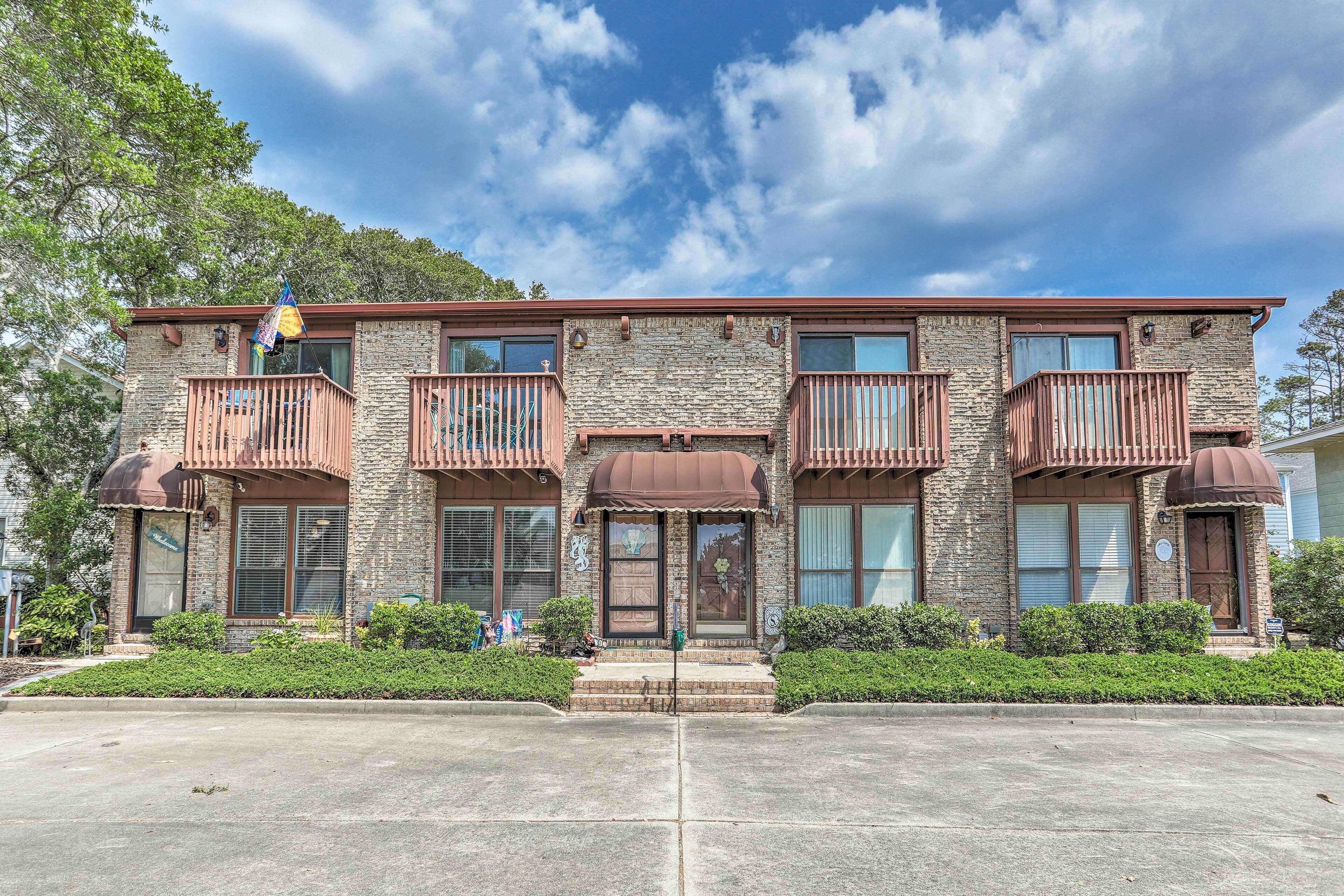 A two-story building with a stone facade, multiple balconies, and a central entrance with a brown awning.