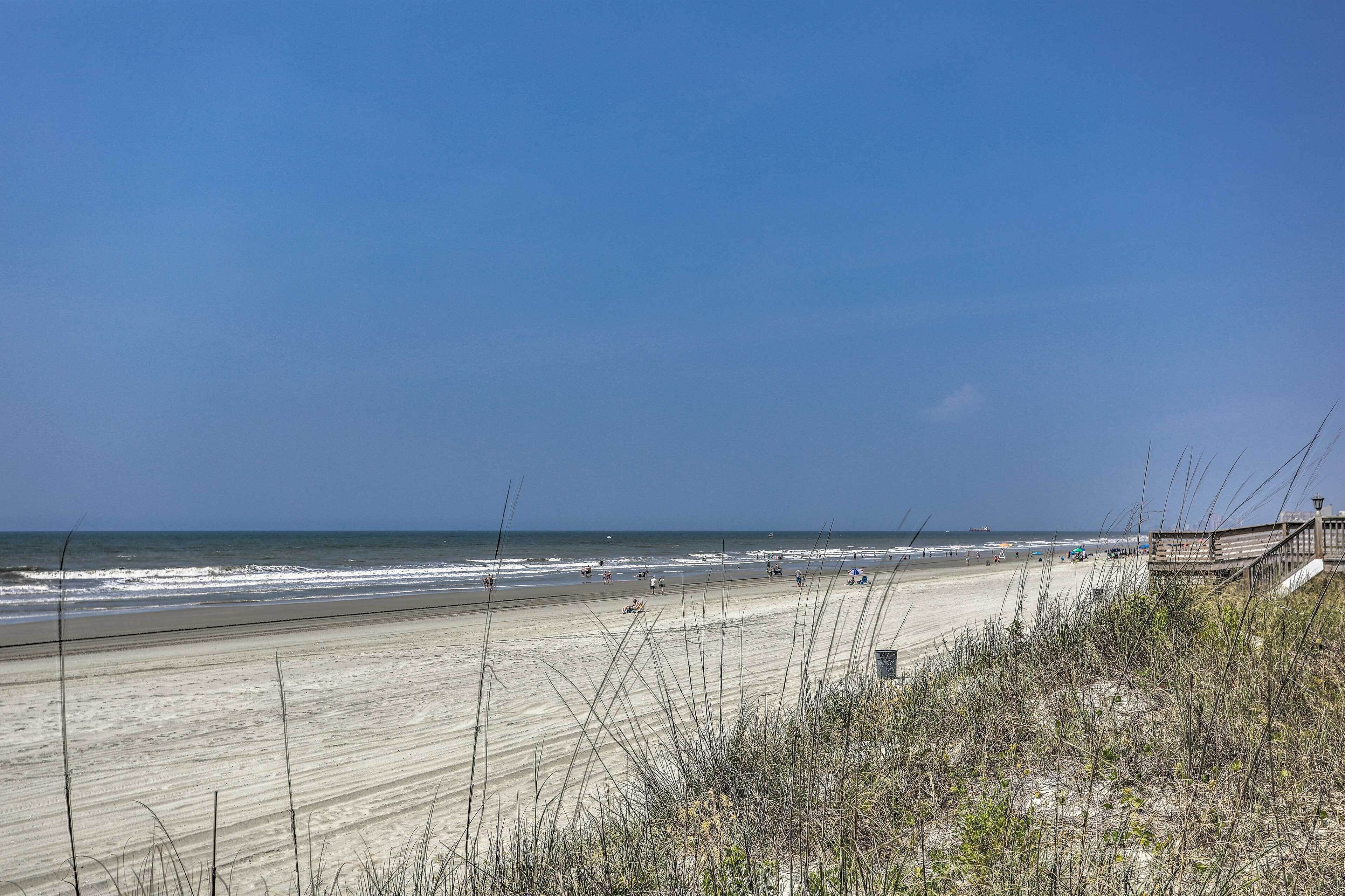 En strand med en træpromenade, sand og havudsigt.