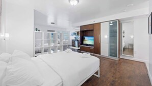 A modern hotel room with a bed, a TV, a kitchenette, and a bathroom.