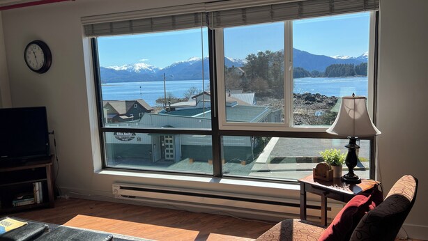 A living room with a large window, a television, a heater, and a lamp. - Studio Downtown Apt. 7 w/ Ocean & Mountain Views. (Sitka)
