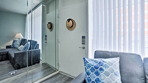 Un salon moderne avec une cloison en verre, un canapé agrémenté de coussins à motifs et une porte sur laquelle est accroché un chapeau.