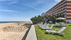 Un hôtel situé en bord de mer, doté d’une promenade en béton, de chaises longues blanches et de parasols.