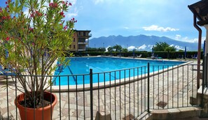 A swimming pool with a metal fence, potted plants, and a view of mountains in the background. - Appartamento 204 Benaco (Tignale)