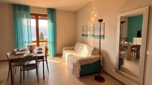A room with a dining table set for four, a sofa, a floor lamp, and a large mirror on the wall.