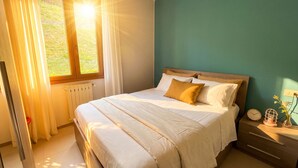 A bedroom with a bed, a window with curtains, a bedside table with a clock, and a radiator.