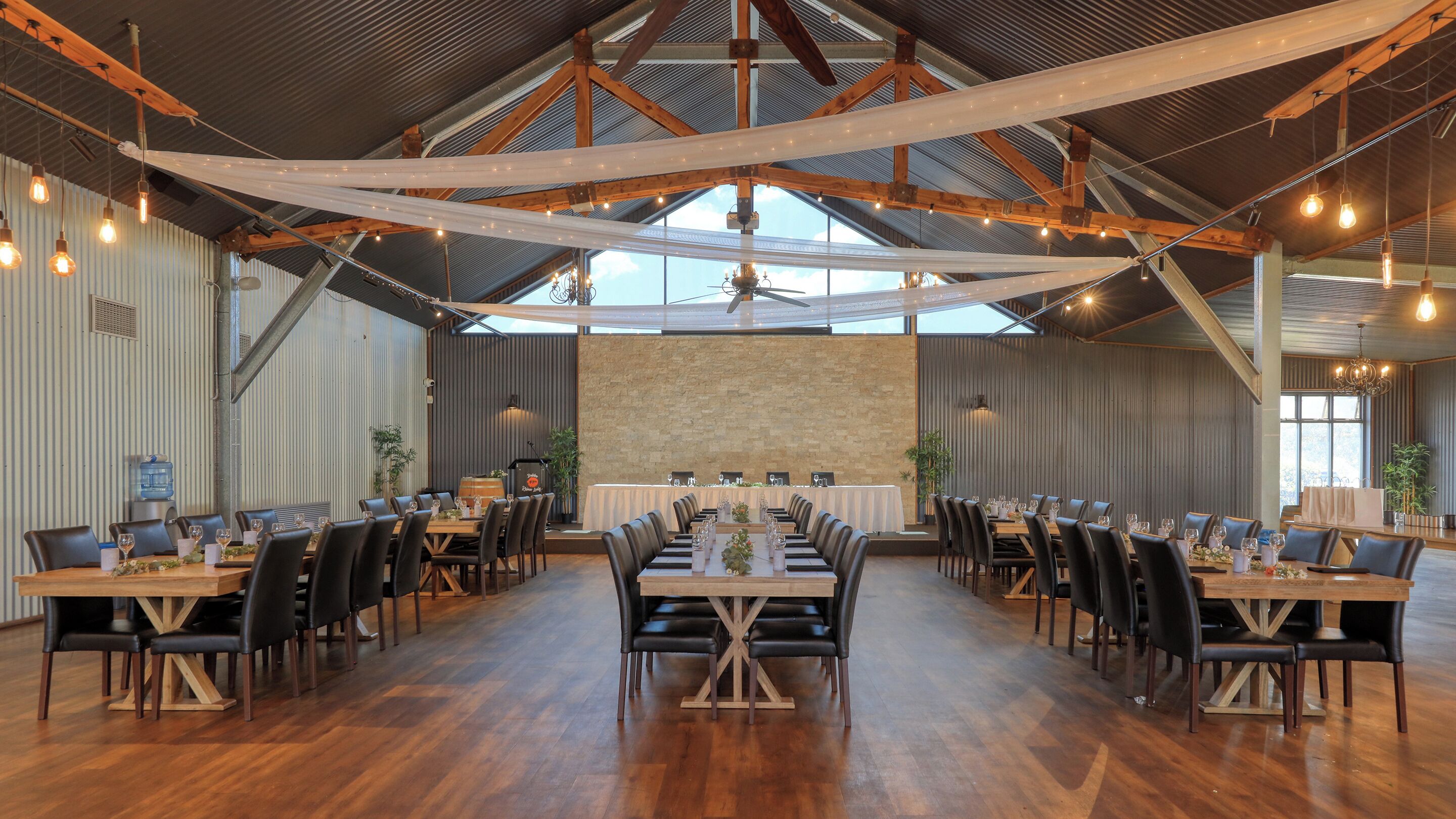 Une vaste salle dotée de hauts plafonds, de poutres en bois et d’une longue table dressée pour le repas.
