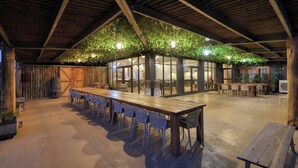 An indoor dining area with a long wooden table and white chairs, surrounded by wooden beams and a ceiling covered with green foliage. - Dubbo Rhino Lodge (Dubbo)