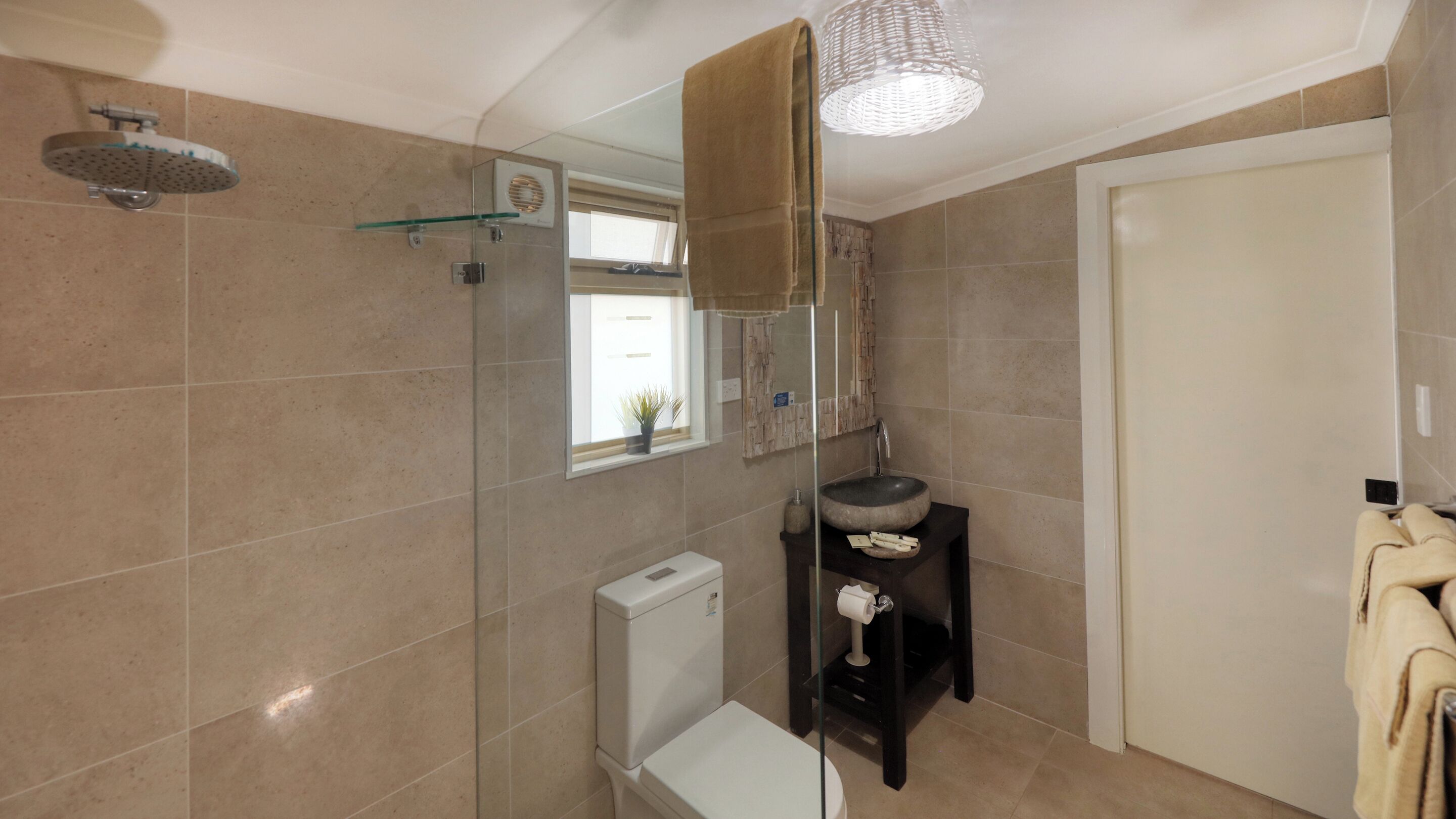 Un baño moderno con cabina de ducha de vidrio, inodoro, lavamanos con un lavabo decorativo y un perchero para toallas.