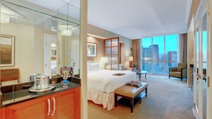 A hotel room with a large bed, a sitting area with a table and chairs, a kitchenette, a large window with a city view, and a mirror reflecting the room. - Signature @ MGM Grand, Lazy River Access, Strip view Penthouse Floor (Las Vegas)