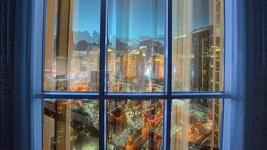 A view through a window with a cityscape at dusk, featuring illuminated buildings and a busy street below. - Signature @ MGM Grand, Lazy River Access, Strip view Penthouse Floor (Las Vegas)