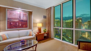A hotel room with a large window offering a city view, a sofa, a glass coffee table, and a painting on the wall. - Signature @ MGM Grand, Lazy River Access, Strip view Penthouse Floor (Las Vegas)