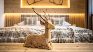 Una escultura de ciervo de madera sobre una mesa frente a una cama con una colcha y almohadas estampadas.