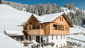 Una cabaña de madera con balcón, rodeada de laderas y árboles cubiertos de nieve.