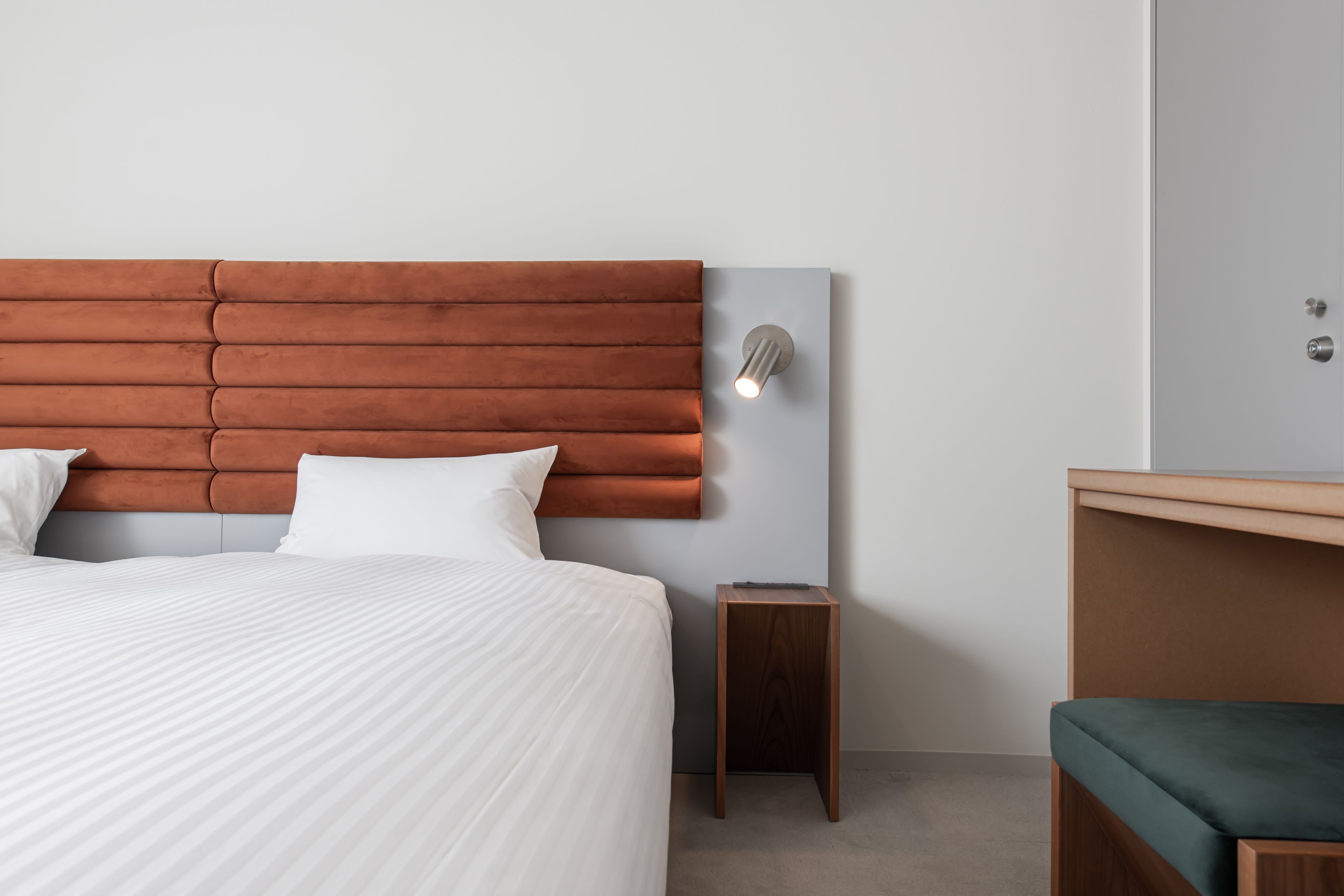 A neatly made bed with white bedding, a wooden headboard, a small bedside table, and a green bench.