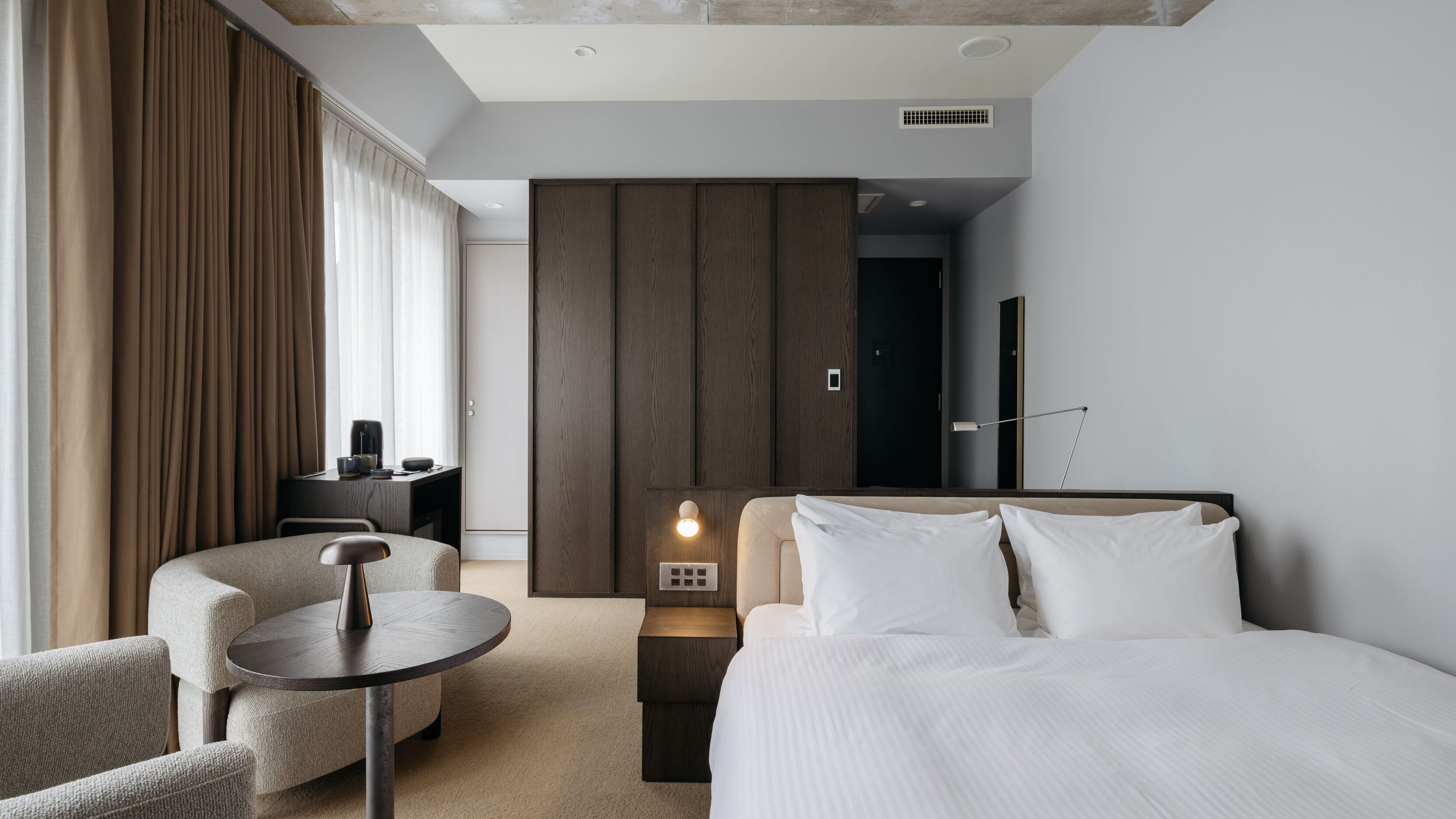 A modern hotel room with a bed, a desk, a chair, and a nightstand.