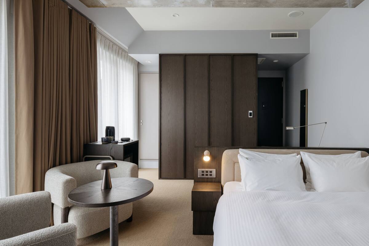 A modern hotel room with a bed, a desk, a chair, and a nightstand.