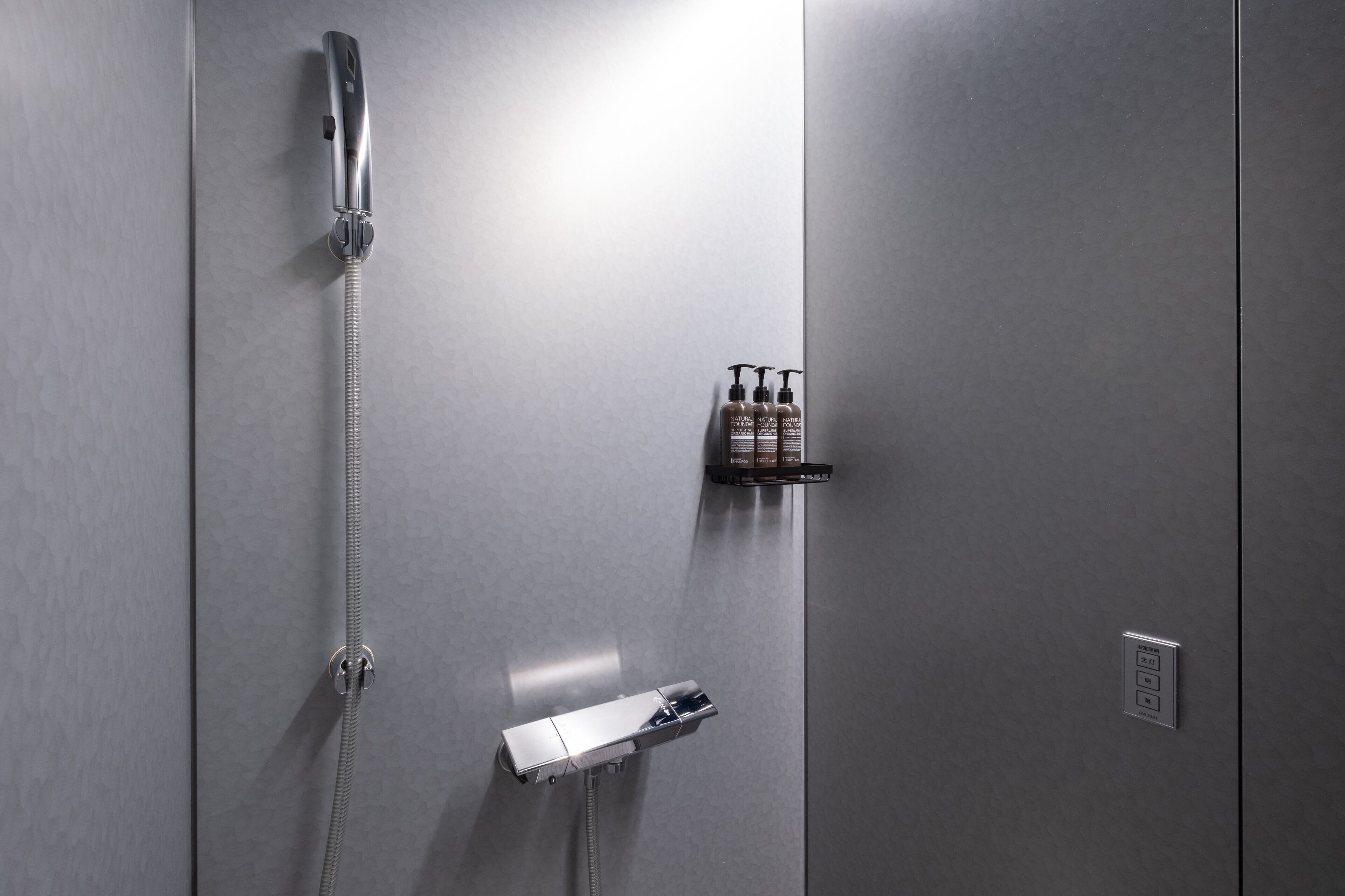 Un bagno moderno con doccia a incasso, soffione a mano e dispenser per sapone.