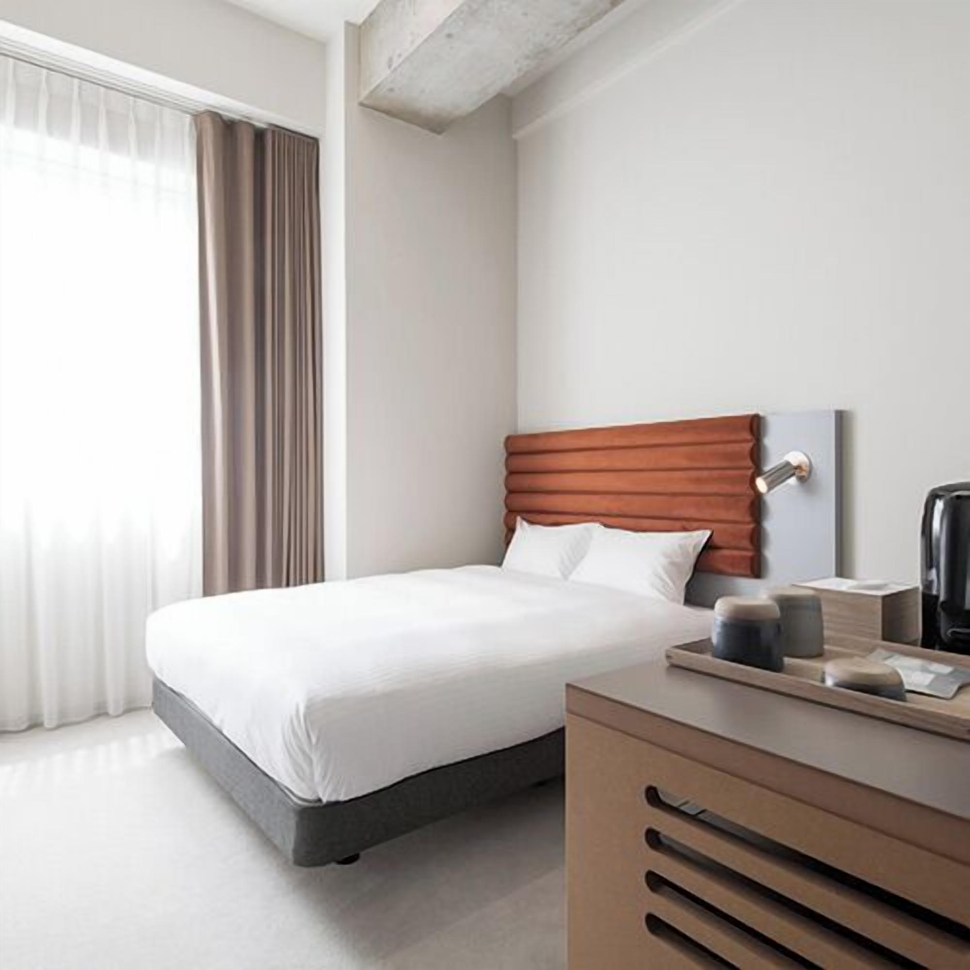 Ein modernes Hotelzimmer mit Bett, einem Holzkapständer, einer Kaffeemaschine und einem fenster mit Vorhängen.