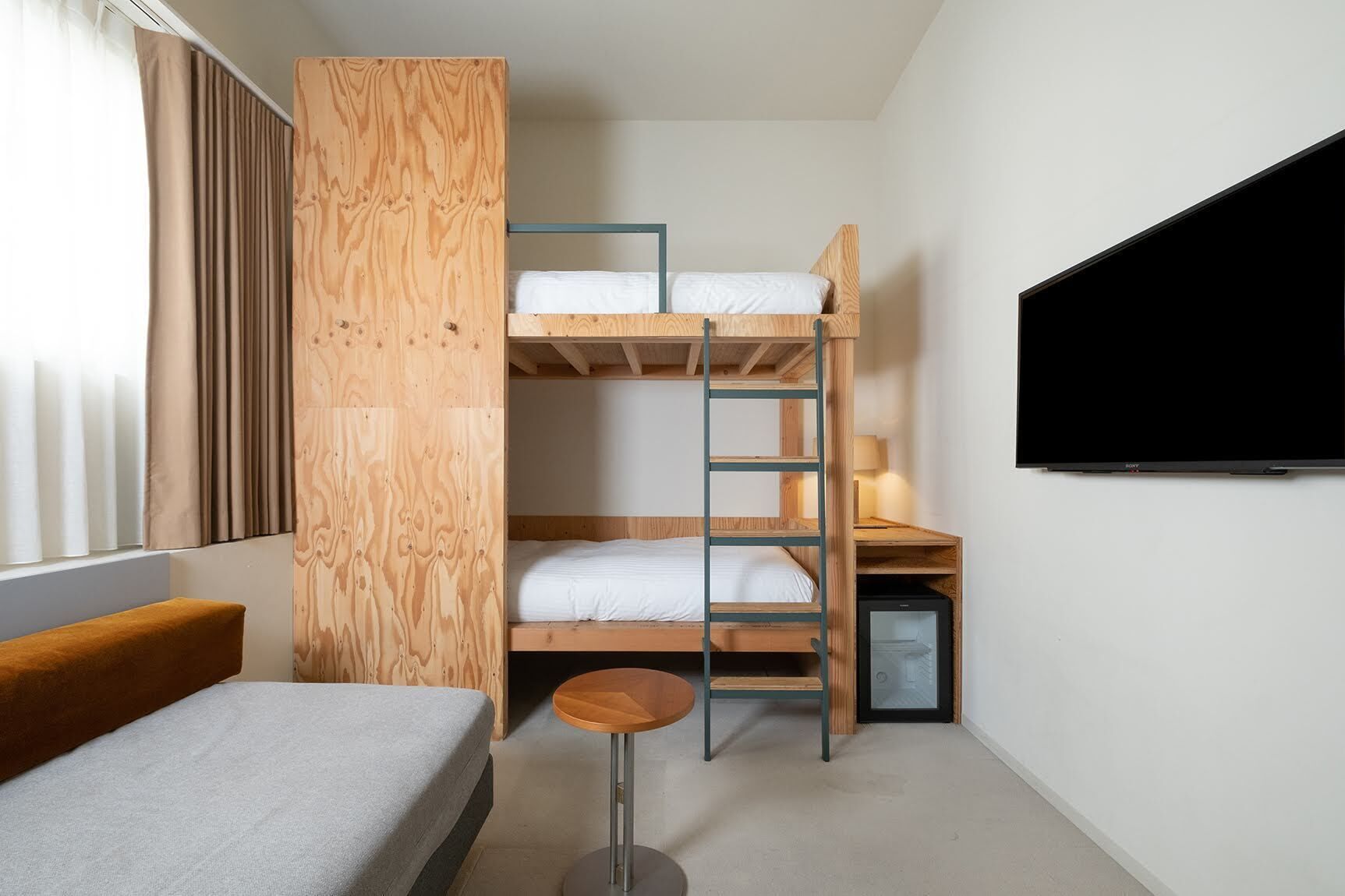 Een kleine kamer met een stapelbed, een bureau, een televisie en een slaapbank.