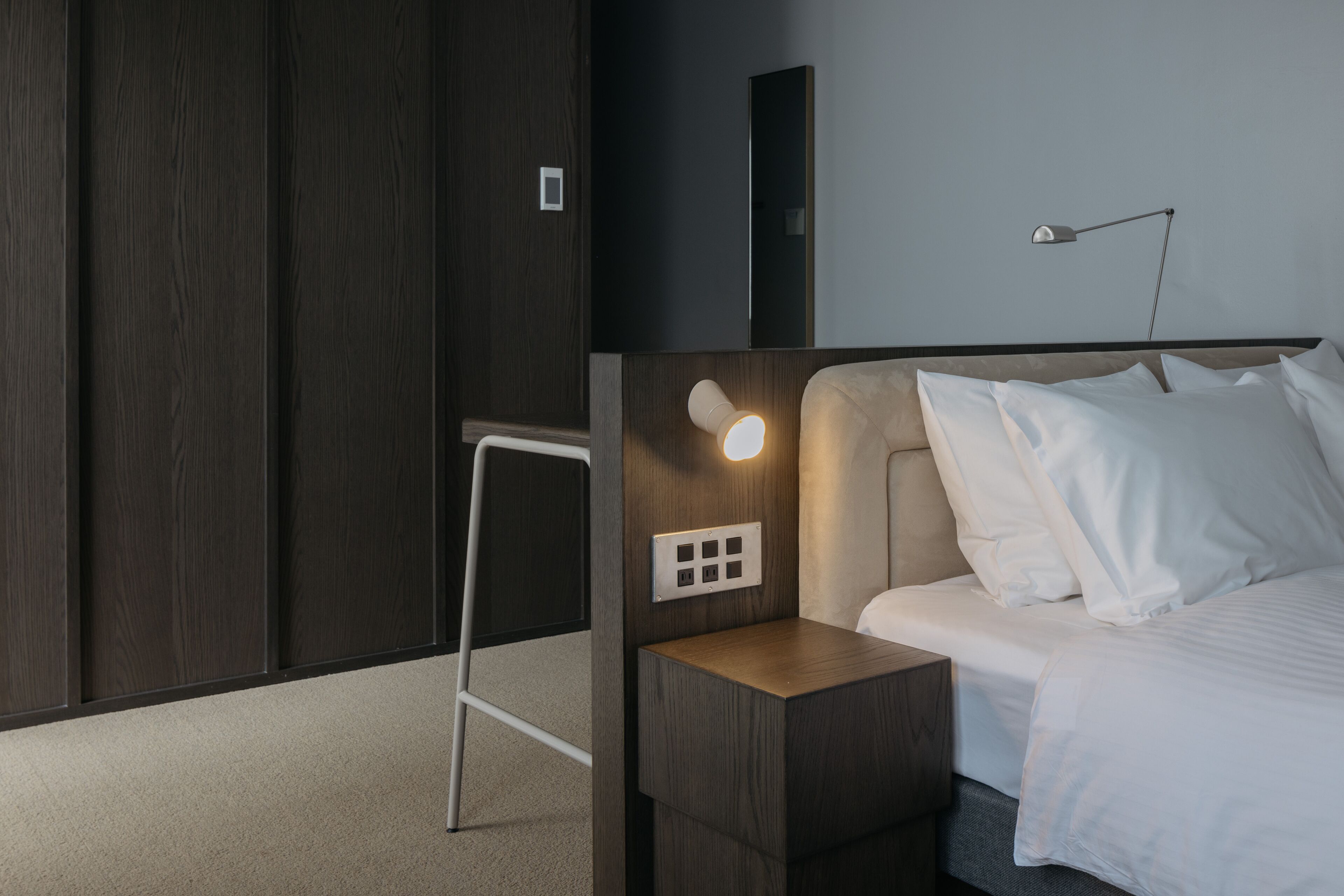 Un dormitorio moderno con cabecera de madera, mesita de noche con lámpara y armario.
