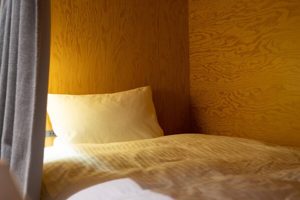 Una cama con almohada blanca y edredón estampado, paredes de madera y una ventana con cortinas.