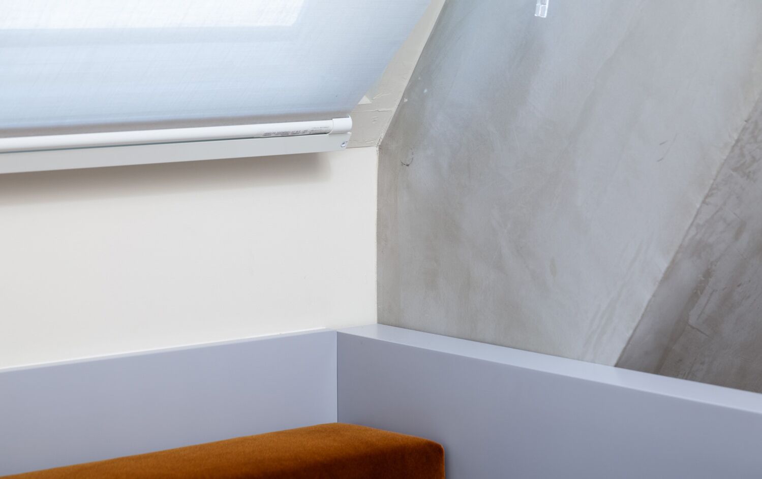 A corner of a room with a skylight, a concrete wall, and a white baseboard.