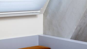 A corner of a room with a skylight, a concrete wall, and a white baseboard.