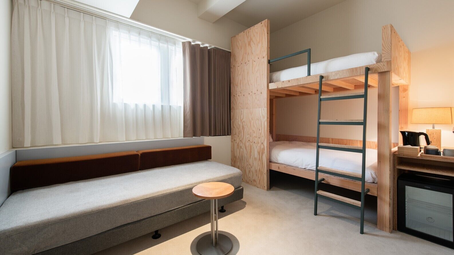 A room with a sofa, bunk beds, a small round table, and a desk with a kettle.