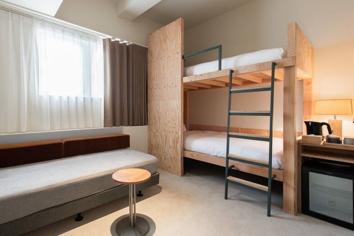 A room with a sofa, bunk beds, a small round table, and a desk with a kettle.