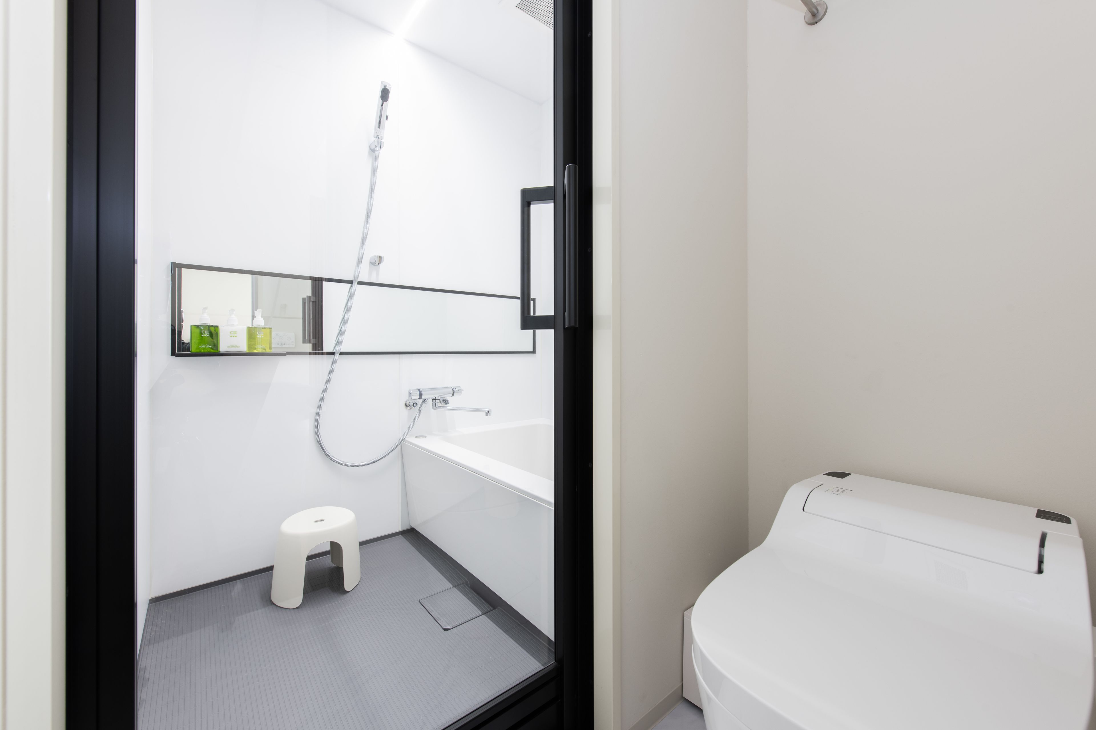 Un baño moderno con ducha, inodoro y un taburete pequeño.