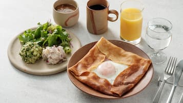 En frukosttallrik med ett pocherat ägg, rostat bröd och sallad, serverad tillsammans med en kopp kaffe, ett glas apelsinjuice och ett glas vatten.