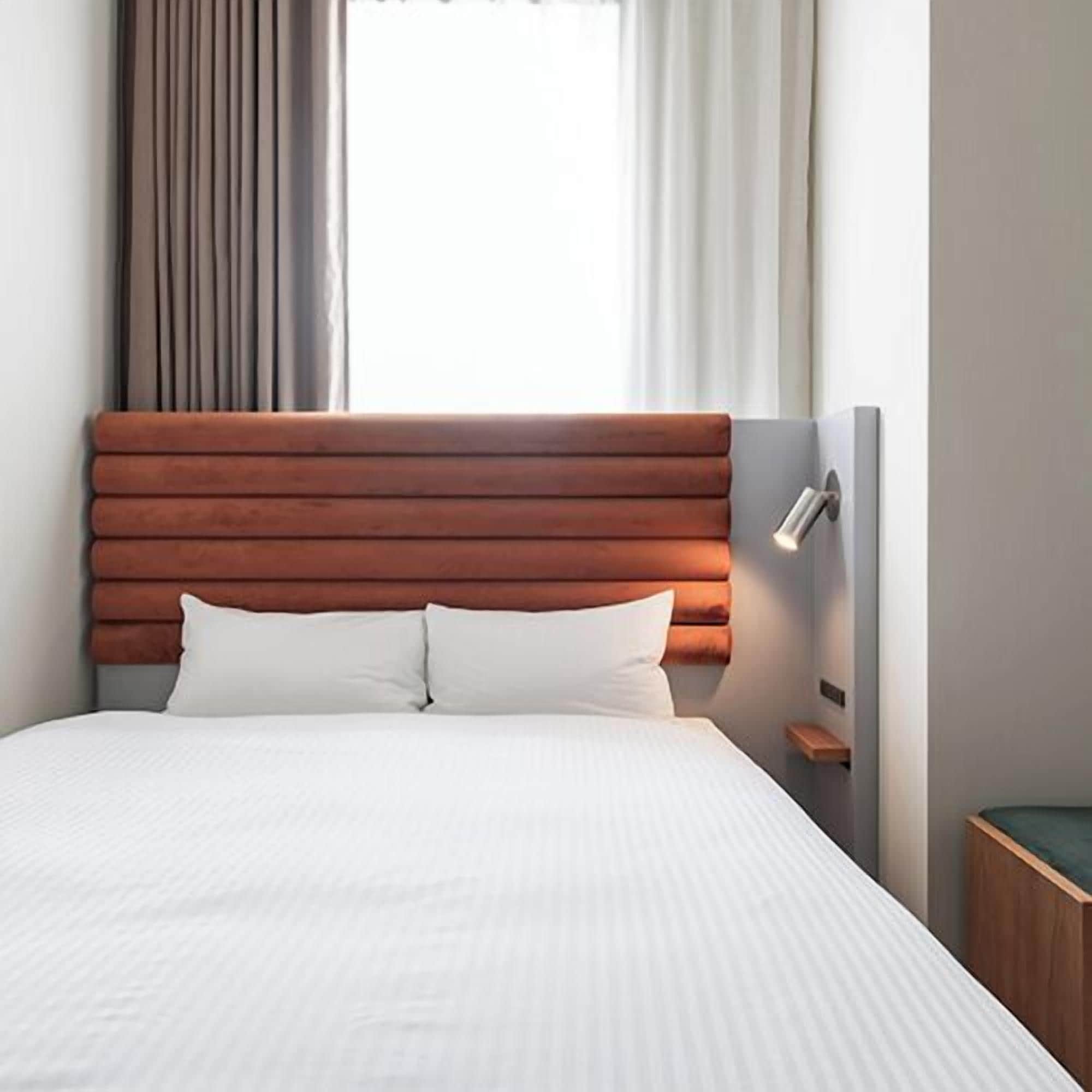 Ein Bett mit Holz Kopfteil, weißer Bettwäsche, einem Nachttisch und einem Fenster mit Vorhängen.
