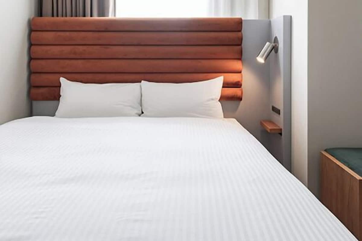 A bed with a wooden headboard, white bedding, a bedside table, and a window with curtains.