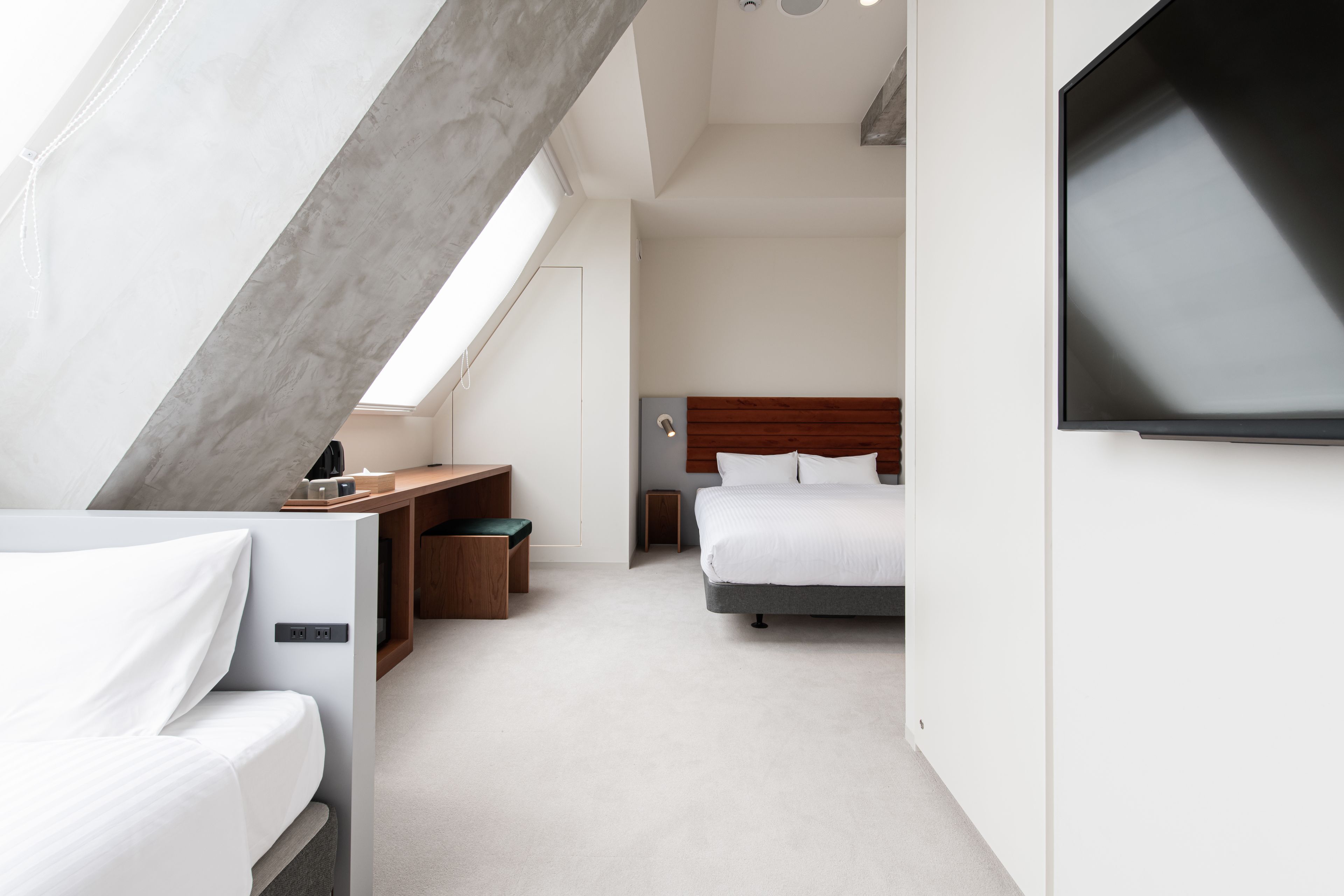 A modern hotel room with a bed, a desk, a television, and a skylight.