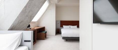 A modern hotel room with a bed, a desk, a television, and a skylight.
