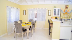 A dining area with a table set for six, a kitchen counter, and a window with curtains. - Ocean View Villa at Coolshade Ocho Rios (St. Ann's Bay)