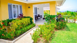 A yellow house with a covered patio, surrounded by lush greenery and a well-maintained lawn. - Ocean View Villa at Coolshade Ocho Rios (St. Ann's Bay)