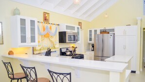 A kitchen with white cabinets, a central island with bar stools, a microwave, stove, and refrigerator. - Ocean View Villa at Coolshade Ocho Rios (St. Ann's Bay)