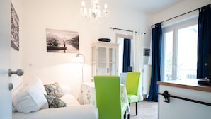 Een kamer met een bed, een eettafel met stoelen, een kast, een kroonluchter en een raam met gordijnen.