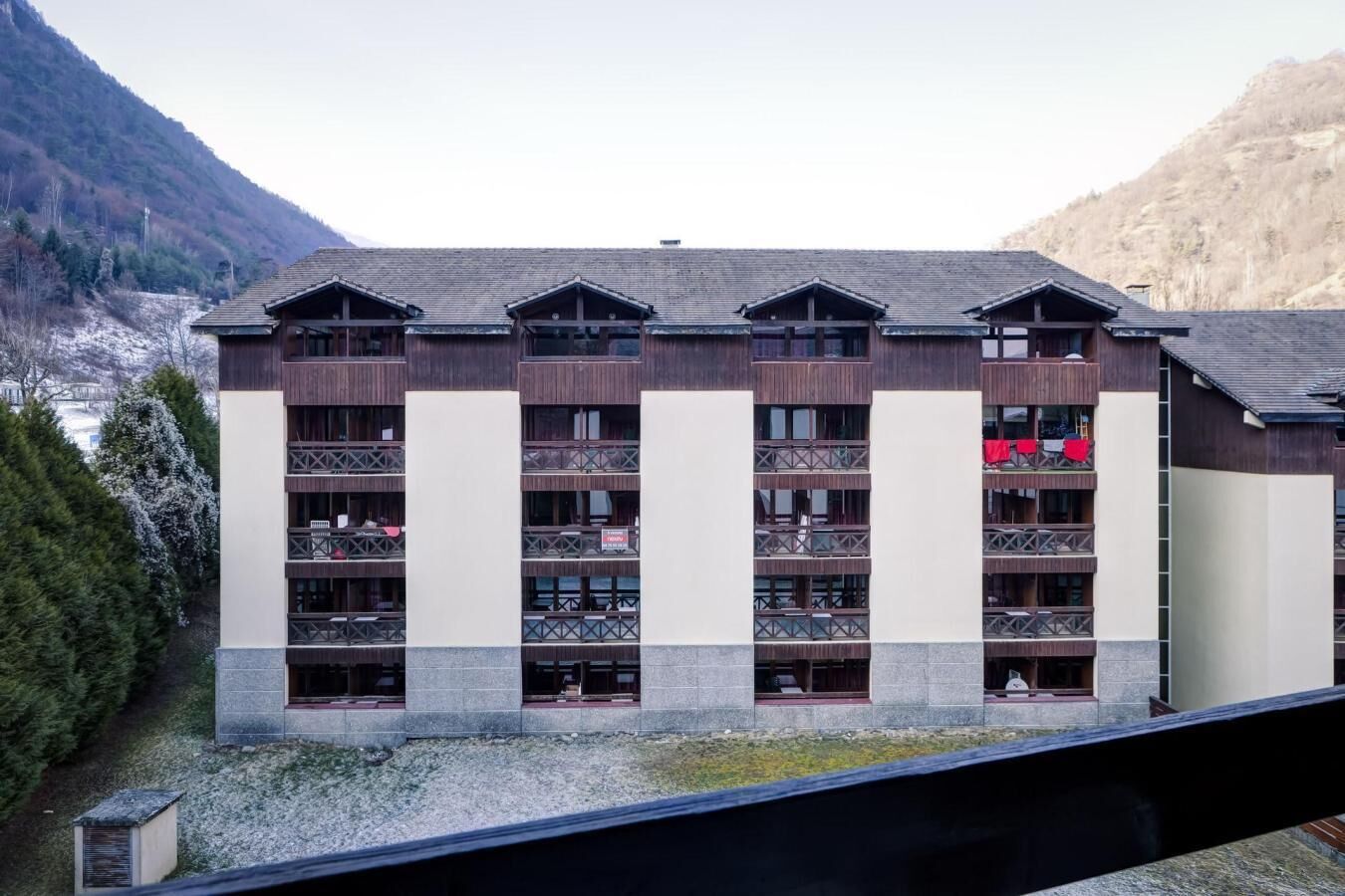 A multi-story hotel with balconies, set against a mountainous backdrop.