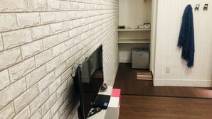 Ett rum med en vit tegelvägg, en platt-TV som är monterad på väggen, ett litet kylskåp och ett trägolv.